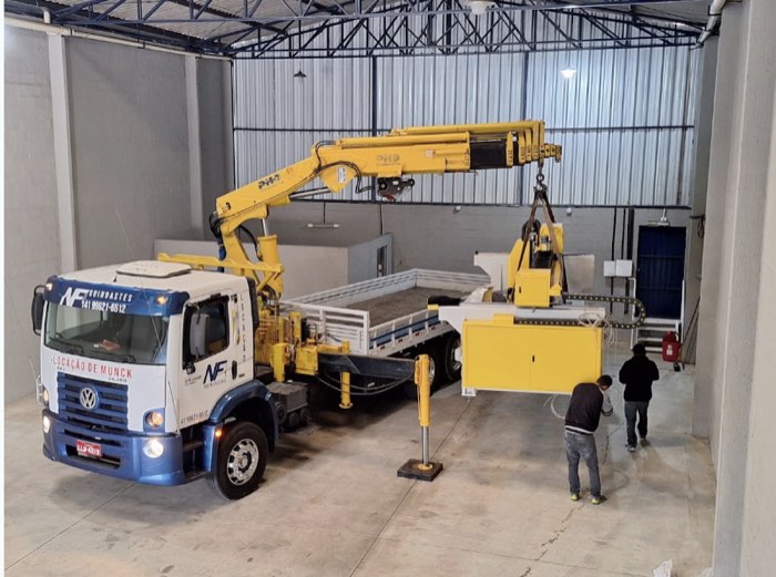 Munck movimentando máquina industrial dentro de galpão